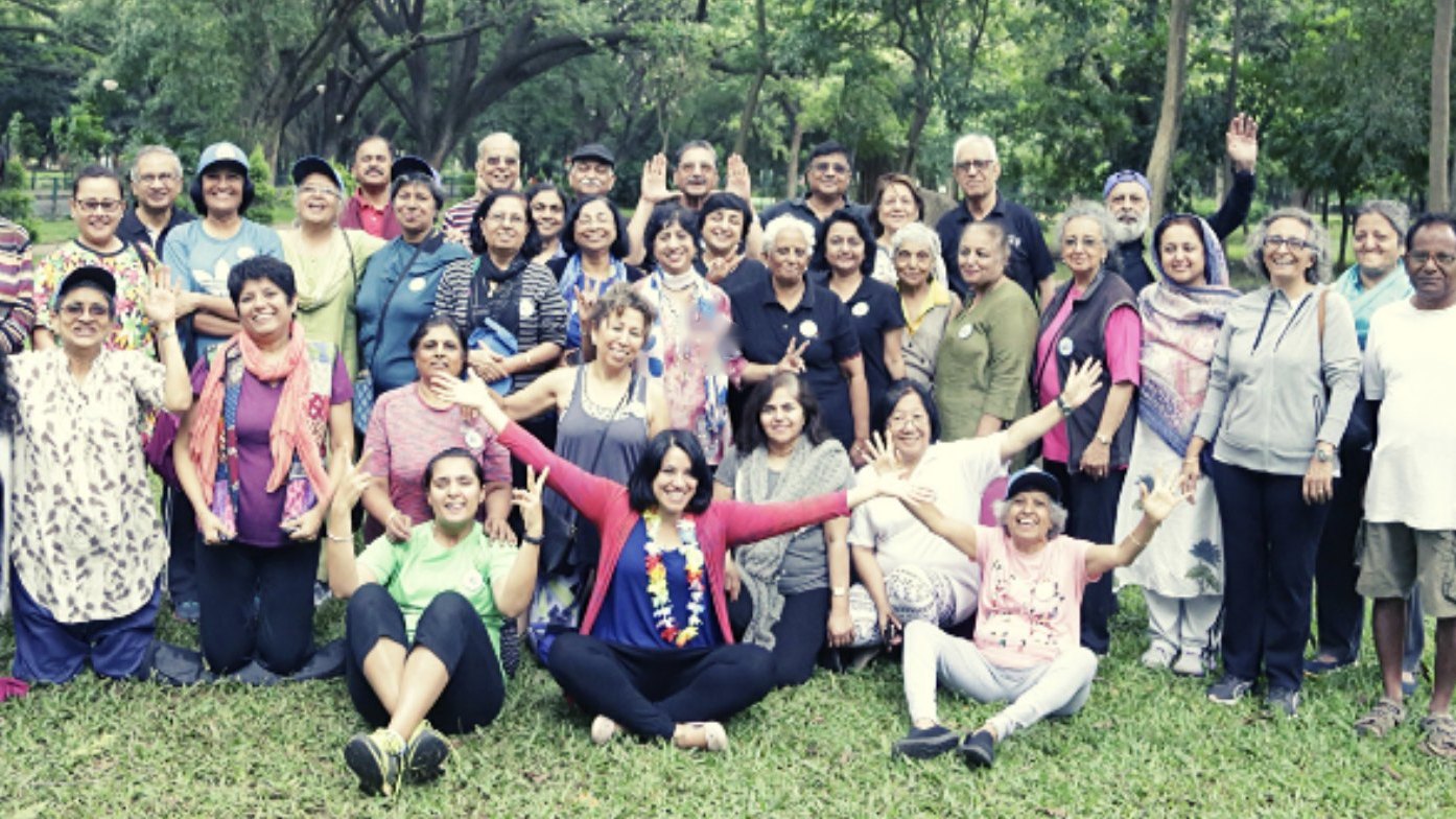 A large, cheerful group of Silver Surfers Club members waving together in a park